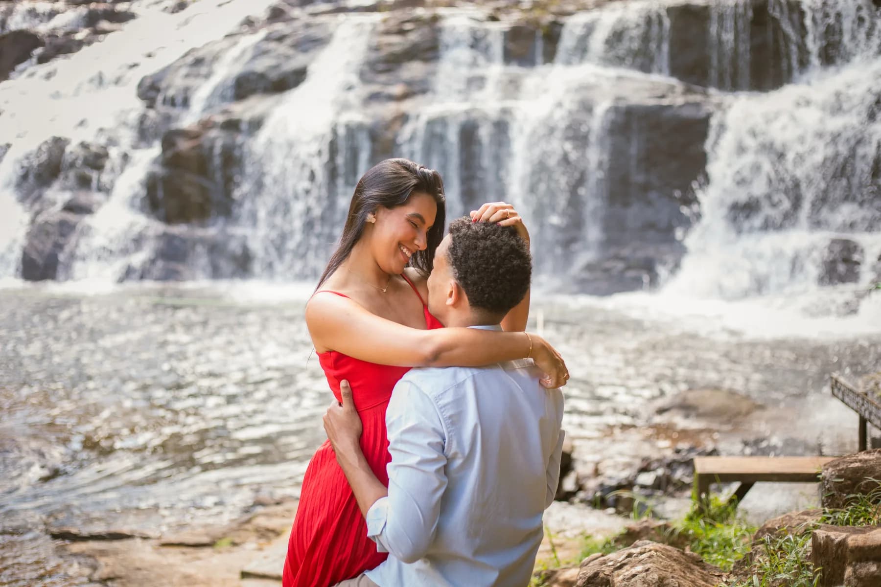 O casal abraçado diante da cachoeira, ela de vestido vermelho