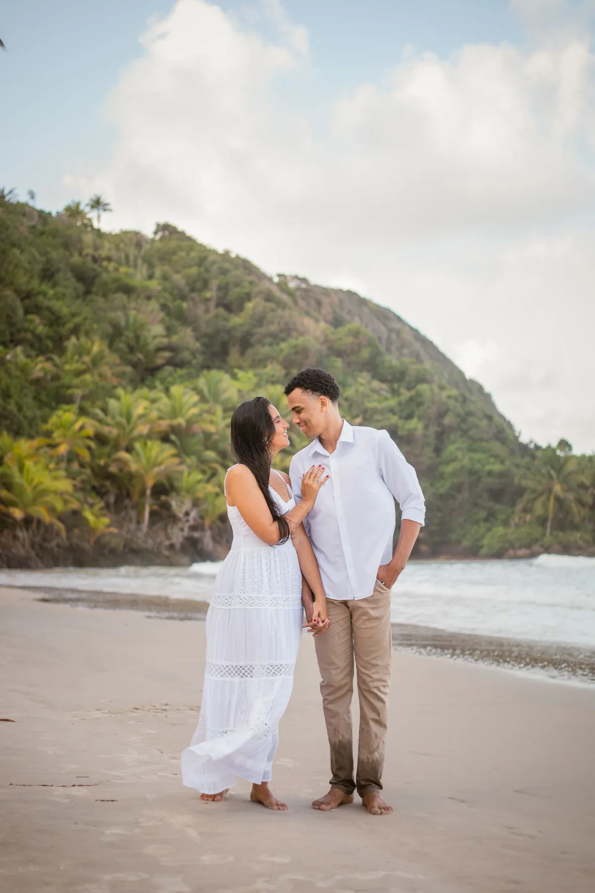 O casal de mãos dadas na praia, olhando um para o outro