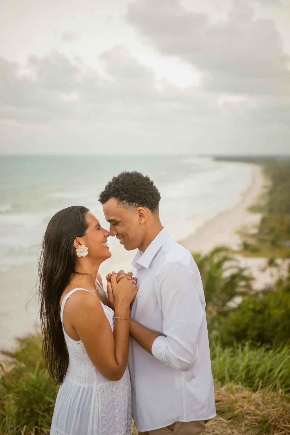 O casal de mãos dadas num mirante, com a faixa de praia ao fundo