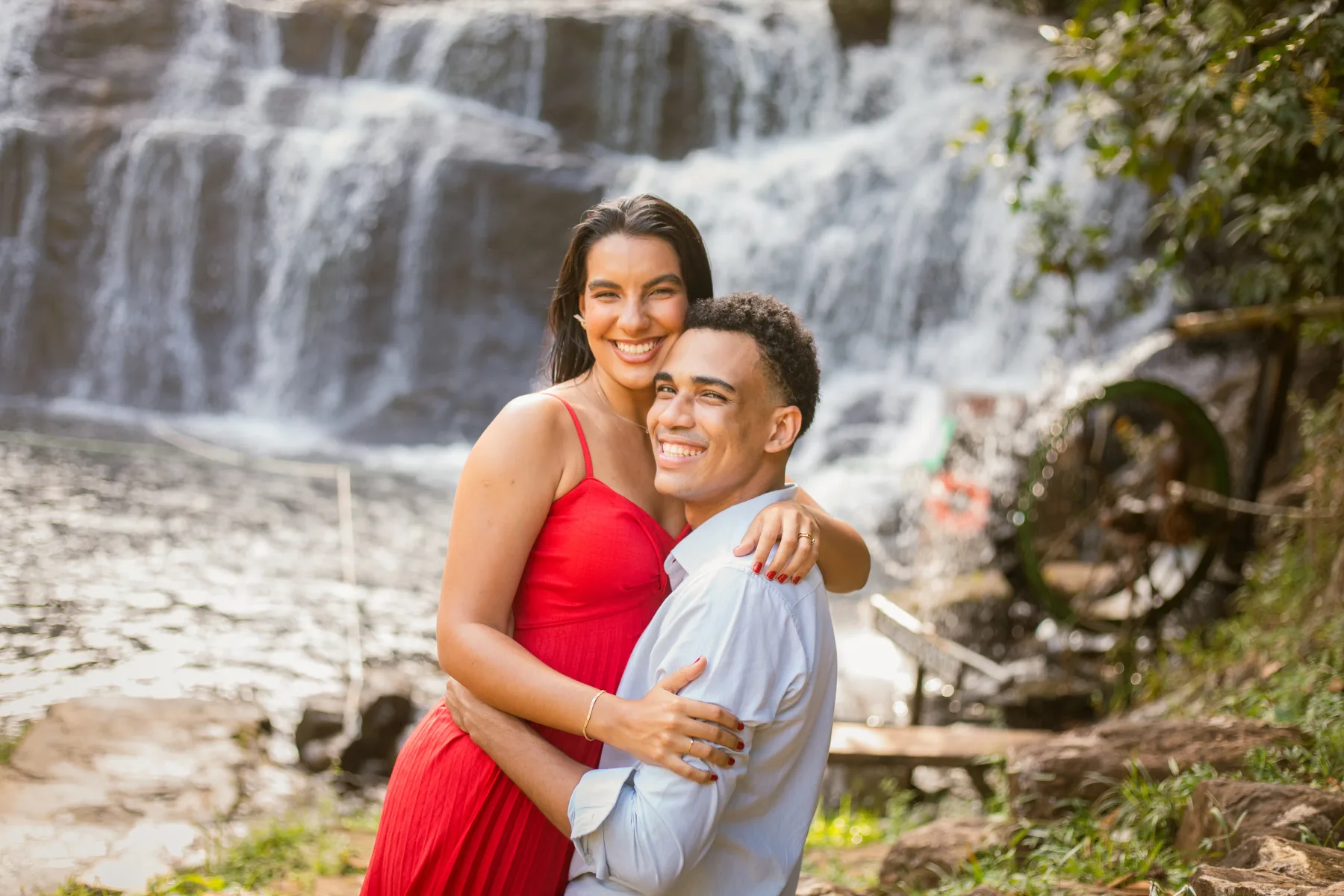 O casal abraçado sorrindo para a câmera, com a cachoeira ao fundo
