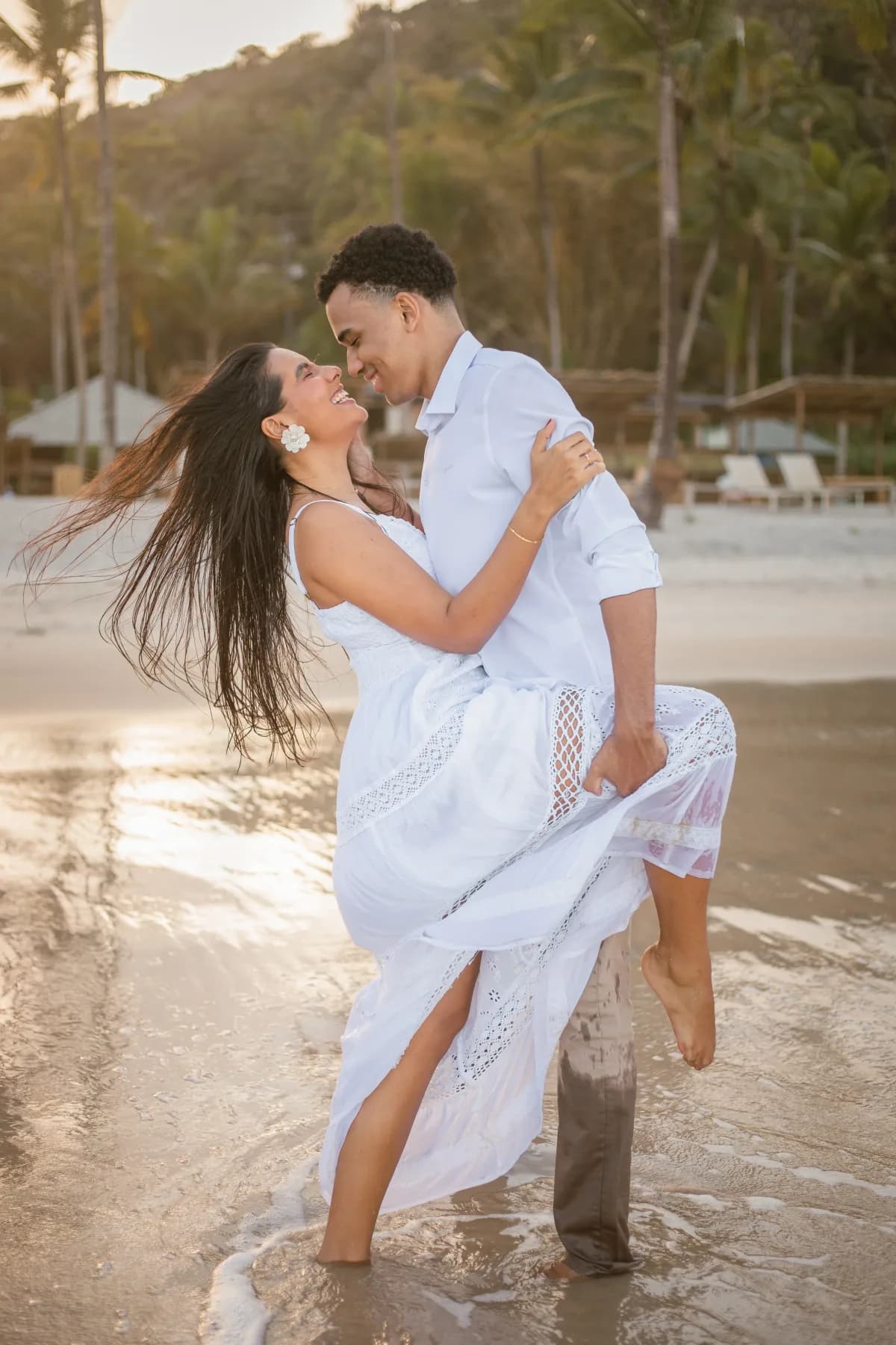 Isaque erguendo Beatriz no colo na beira do mar, os dois rindo